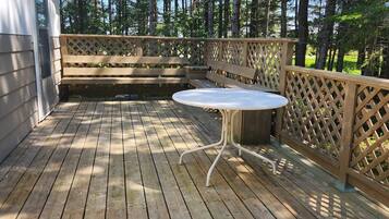 A wooden deck with a table and benches, surrounded by a wooden fence and tall trees.