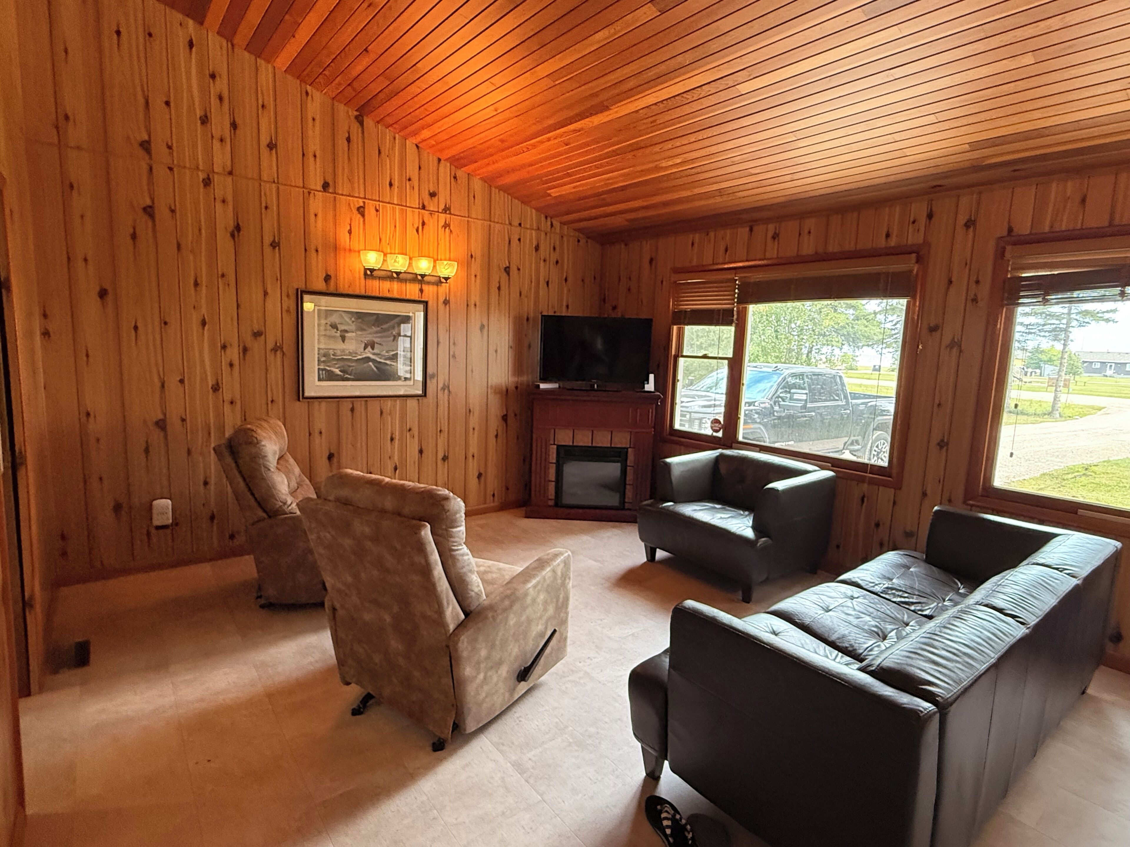 A wooden-paneled room with a fireplace, a television, and a seating area with two sofas and a recliner.