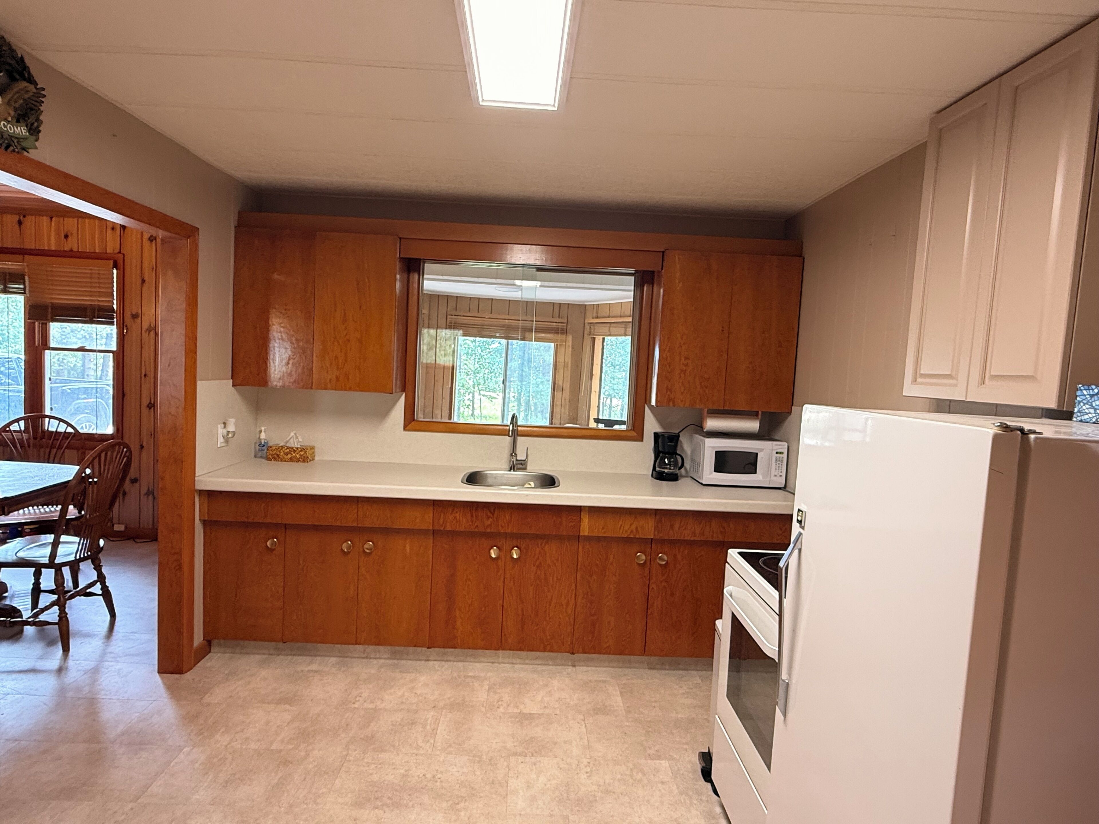 A kitchen with wooden cabinets, a white countertop, a sink, a microwave, and a refrigerator.