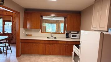 A kitchen with wooden cabinets, a white countertop, a sink, a microwave, and a refrigerator.