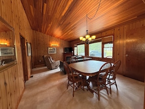 A wooden interior with a dining table, chairs, a television, and framed pictures on the walls.