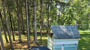 A small wooden structure with a sloped roof, possibly a shed or a playhouse, situated on a concrete patio surrounded by trees. - Modern Rustic Cabin in Balaton Beach with Lake Access & Firepit (Balaton Beach)