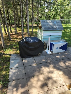 A small wooden structure with a sloped roof, possibly a shed or a playhouse, situated on a concrete patio surrounded by trees. - Modern Rustic Cabin in Balaton Beach with Lake Access & Firepit (Balaton Beach)