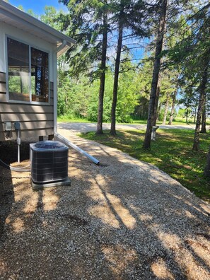 A residential property with a gravel driveway leading to a house, surrounded by trees and a clear sky.