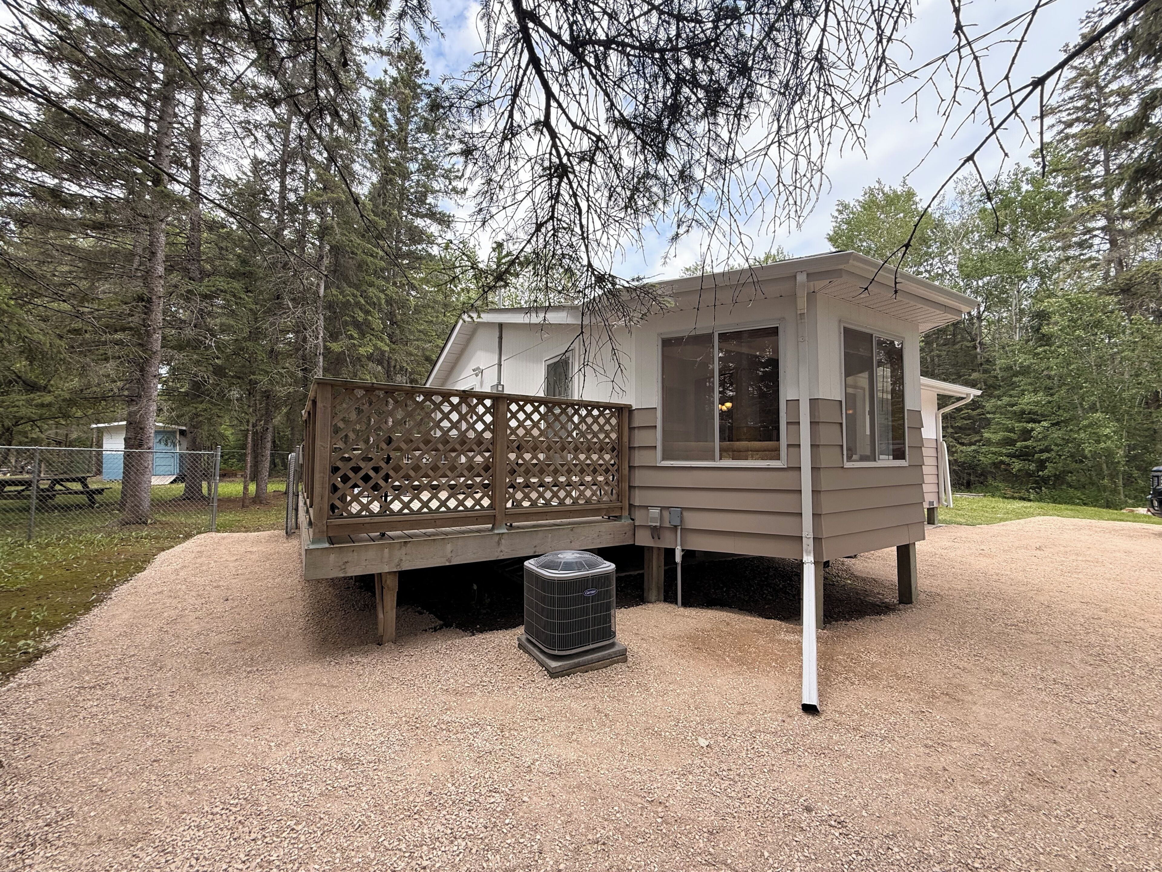 A cabin with a deck, a small shed, and a gravel driveway.