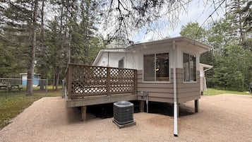 A cabin with a deck, a small shed, and a gravel driveway.