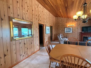 Ein Zimmer mit Holzwänden, einem Esstisch, Stühlen, einem Kamin und einem Fernseher.