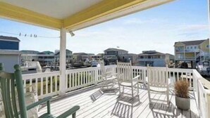 A covered outdoor deck with white railings, chairs, and a potted plant. - Canal-front 3BR, 2BA retreat with dock, WiFi, grill, and dog-friendly comfort. (Supply)