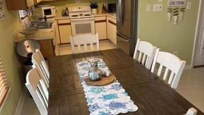 A dining area with a wooden table, white chairs, and a ceiling fan. - Canal-front 3BR, 2BA retreat with dock, WiFi, grill, and dog-friendly comfort. (Supply)
