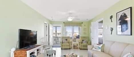 A living room with a flat-screen TV, a coffee table, a sofa, and a dining area with chairs.