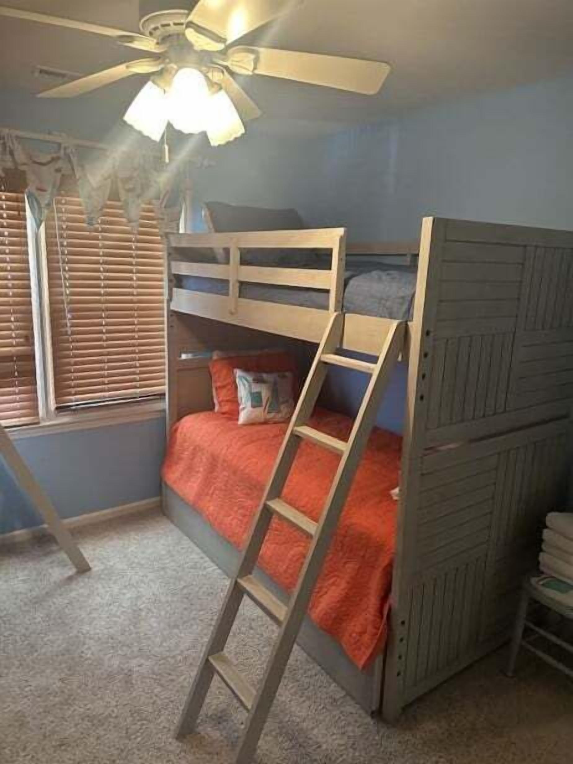 A bunk bed with a ladder, a ceiling fan, and a window with blinds.