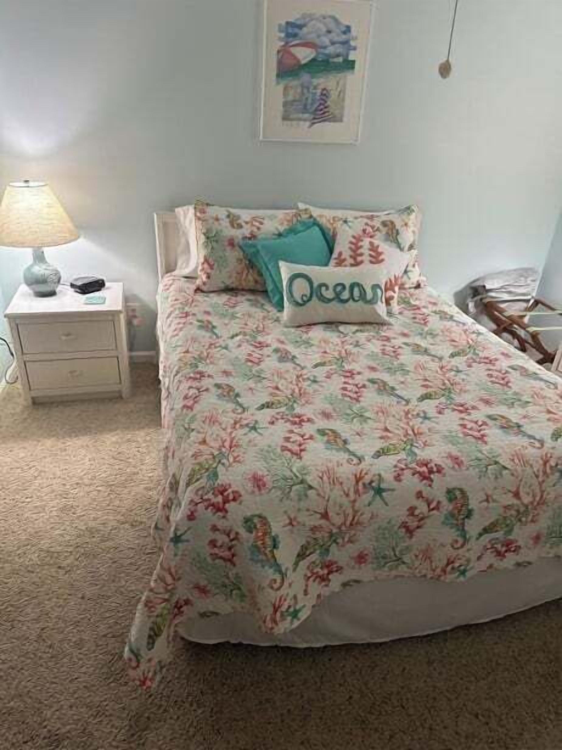 Un dormitorio con una colcha estampada, una mesita de noche con lámpara y un cuadro en la pared.