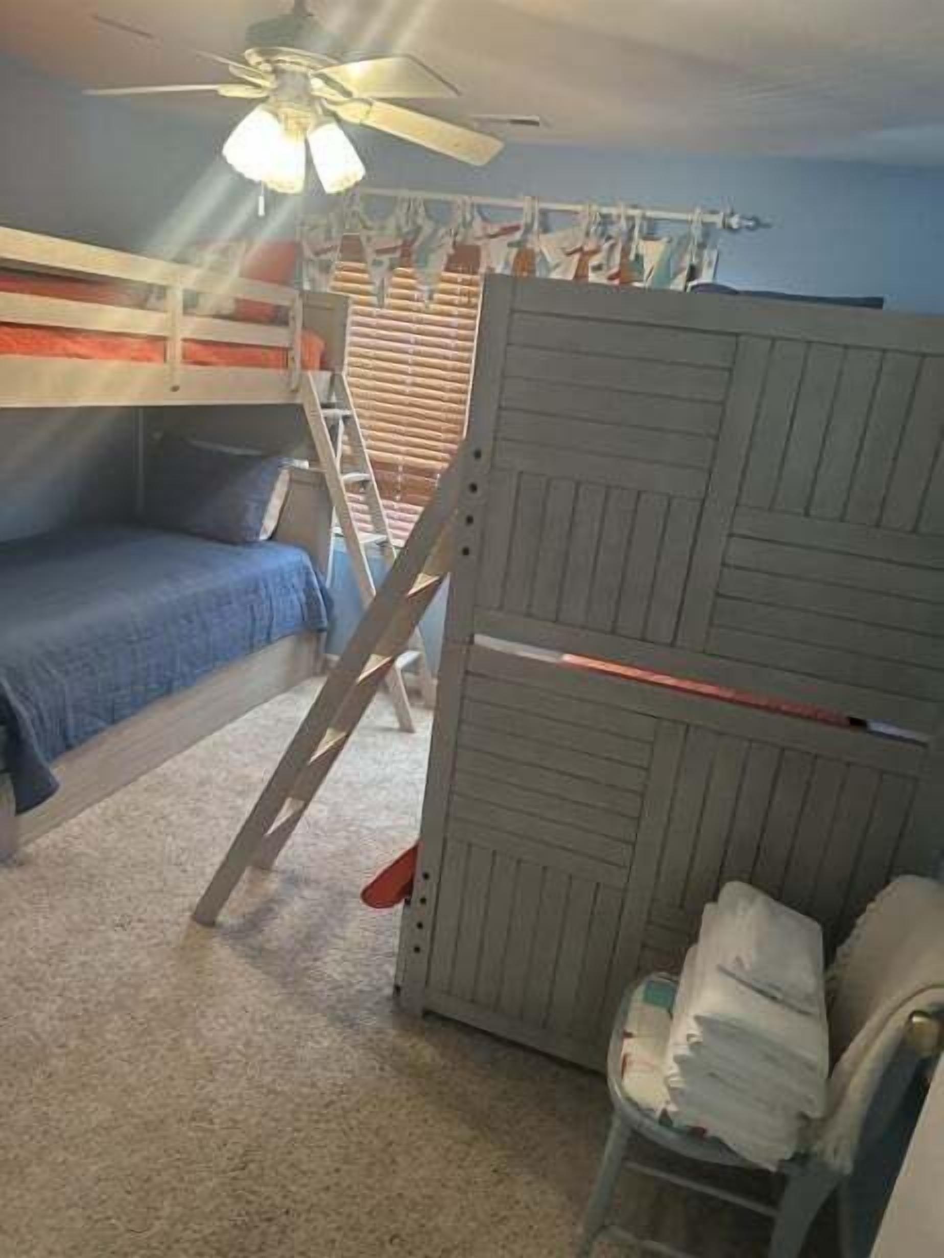 A bunk bed with a ladder, a ceiling fan, and a window with blinds.