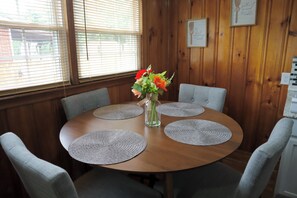 A round wooden table with four grey placemats, surrounded by four grey upholstered chairs. A vase with flowers is placed in the center of the table. - Plan a stay at Westchester Cottage (Charlotte)