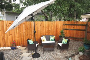 An outdoor patio area with a wooden fence, a table and chairs, and a large umbrella. - Plan a stay at Westchester Cottage (Charlotte)