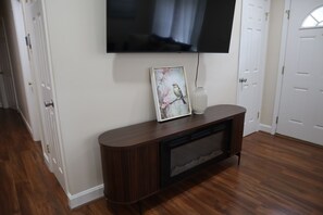 Ein Zimmer mit einem flachbildfernseher an der Wand, einem gerahmten Vogelbild auf einem Regal und einer Vase.