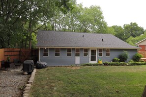 A residential house with a grey roof, a front porch, and a small front yard with a lawn and a wooden fence. - Plan a stay at Westchester Cottage (Charlotte)