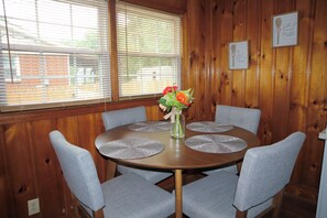 A wooden-paneled room with a round table and four grey chairs.