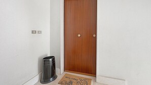 Puerta de madera cerrada con felpudo y un bote de basura a un lado.