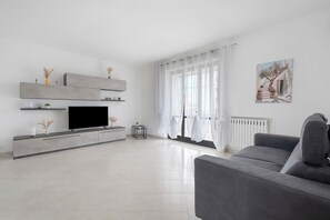 A modern living room with a flat-screen TV, grey sofa, and a painting on the wall.