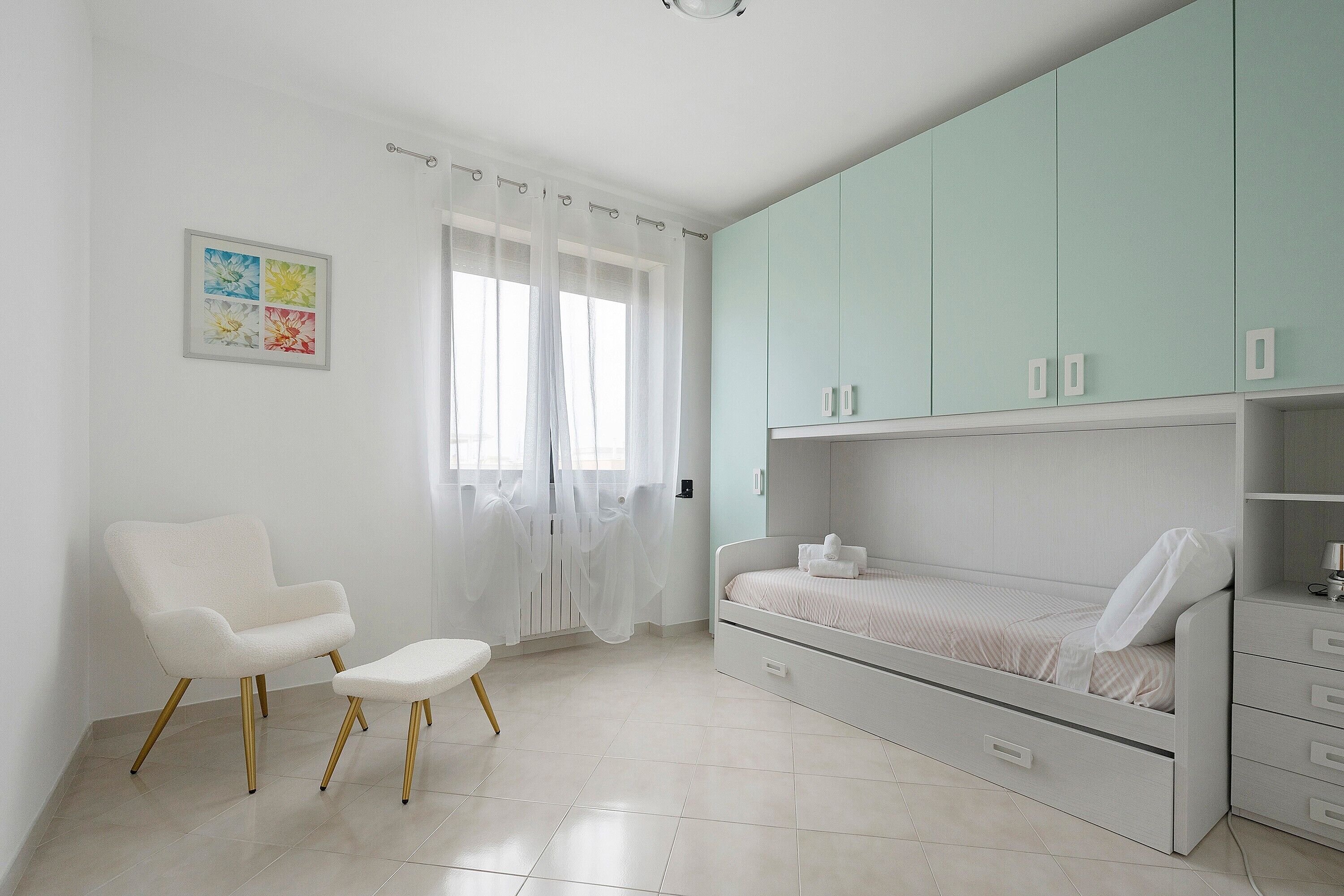 A bedroom with a bed, a chair, a cabinet, and a window with curtains.