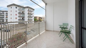 Un balcón con vista a edificios de apartamentos, piso de baldosas y barandilla blanca.