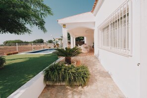 A white building with a pool, a patio, and a fenced garden area.