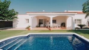 Una propiedad residencial con piscina, un patio amueblado al aire libre y fachada blanca.
