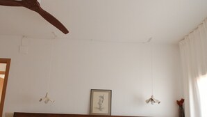 Un dormitorio con una cama, un ventilador de techo, un cuadro en la pared y una ventana con cortinas.