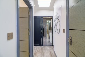 A hallway with a modern design, featuring a door with a glass panel, a wall-mounted light fixture, and a visible washing machine. - Amazing 6 Bed House
Sleeps 14 | Private Parking | EV Charger | Long Stays (London)