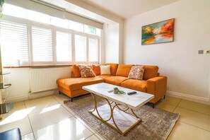Uma sala de estar moderna com sofá seccional, uma mesa de centro de mármore e uma grande janela com persianas.