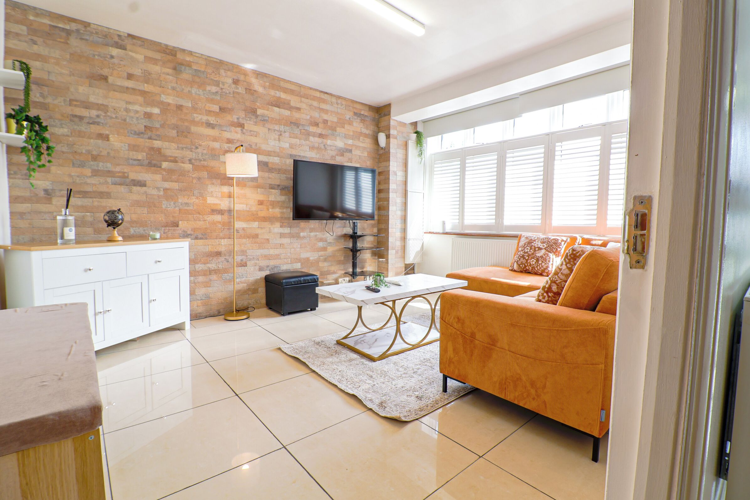 Ein modernes Wohnzimmer mit Backsteinwand, Flachbildfernseher, Sofa, Couchtisch und weißem Schrank.