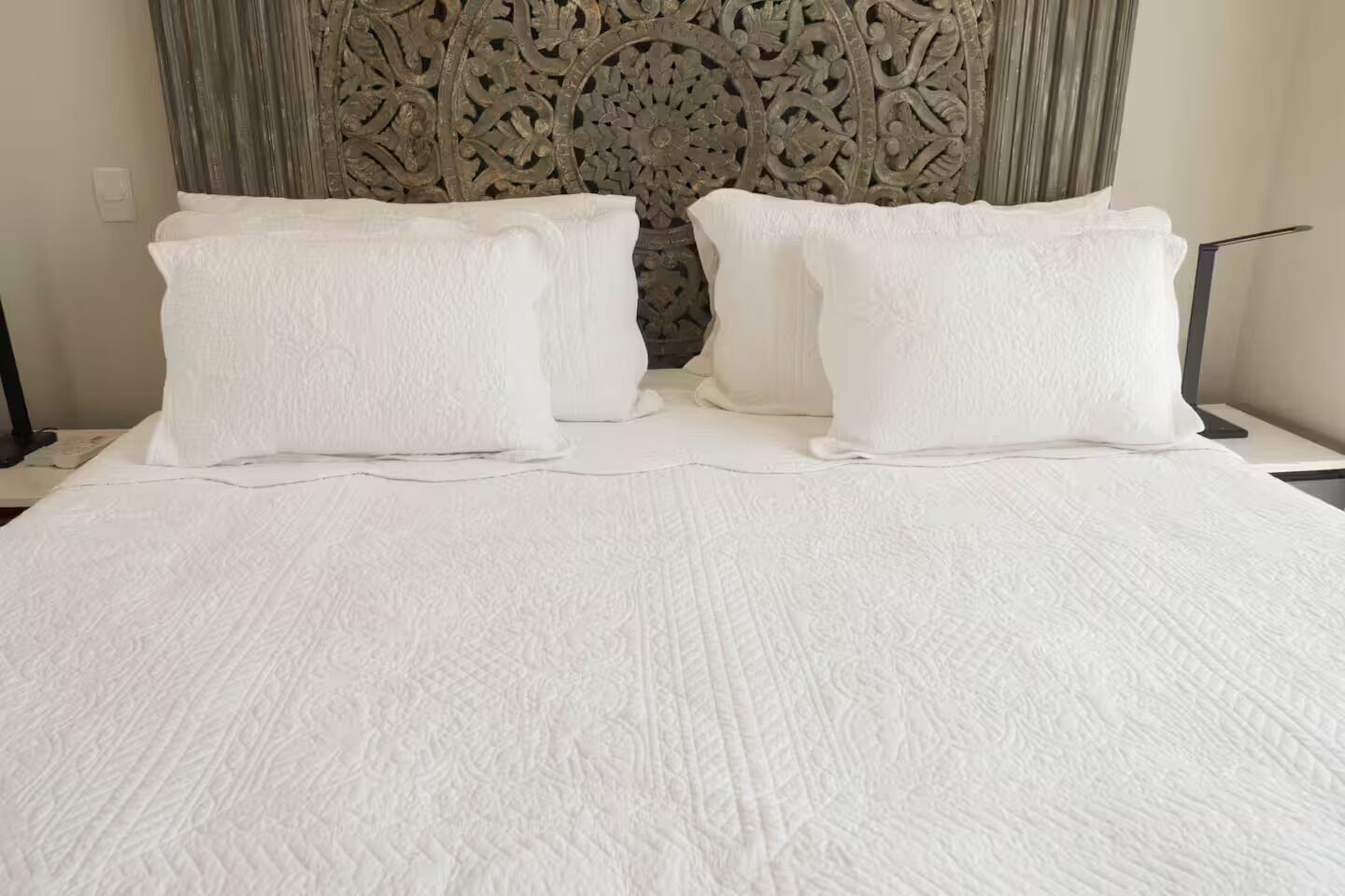A bed with a textured white bedspread and two pillows, set against a backdrop of a decorative headboard.