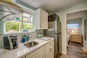 A kitchen with a refrigerator, a coffee maker, and a window with a view of greenery. - 216 Pearl Cozy Pet Friendly Apartment near Beach (Fort Myers Beach)