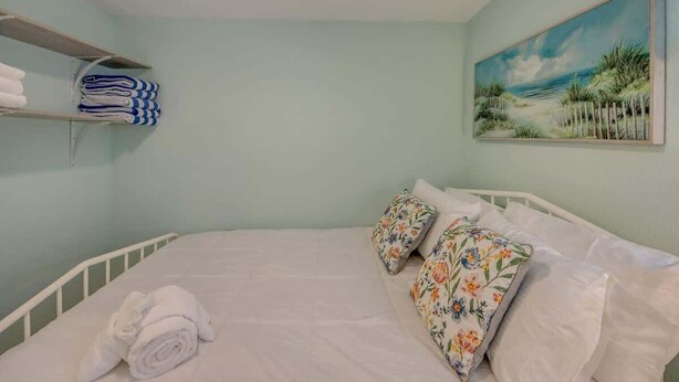 Una camera da letto con un letto, cuscini, un quadro e uno scaffale con asciugamani.