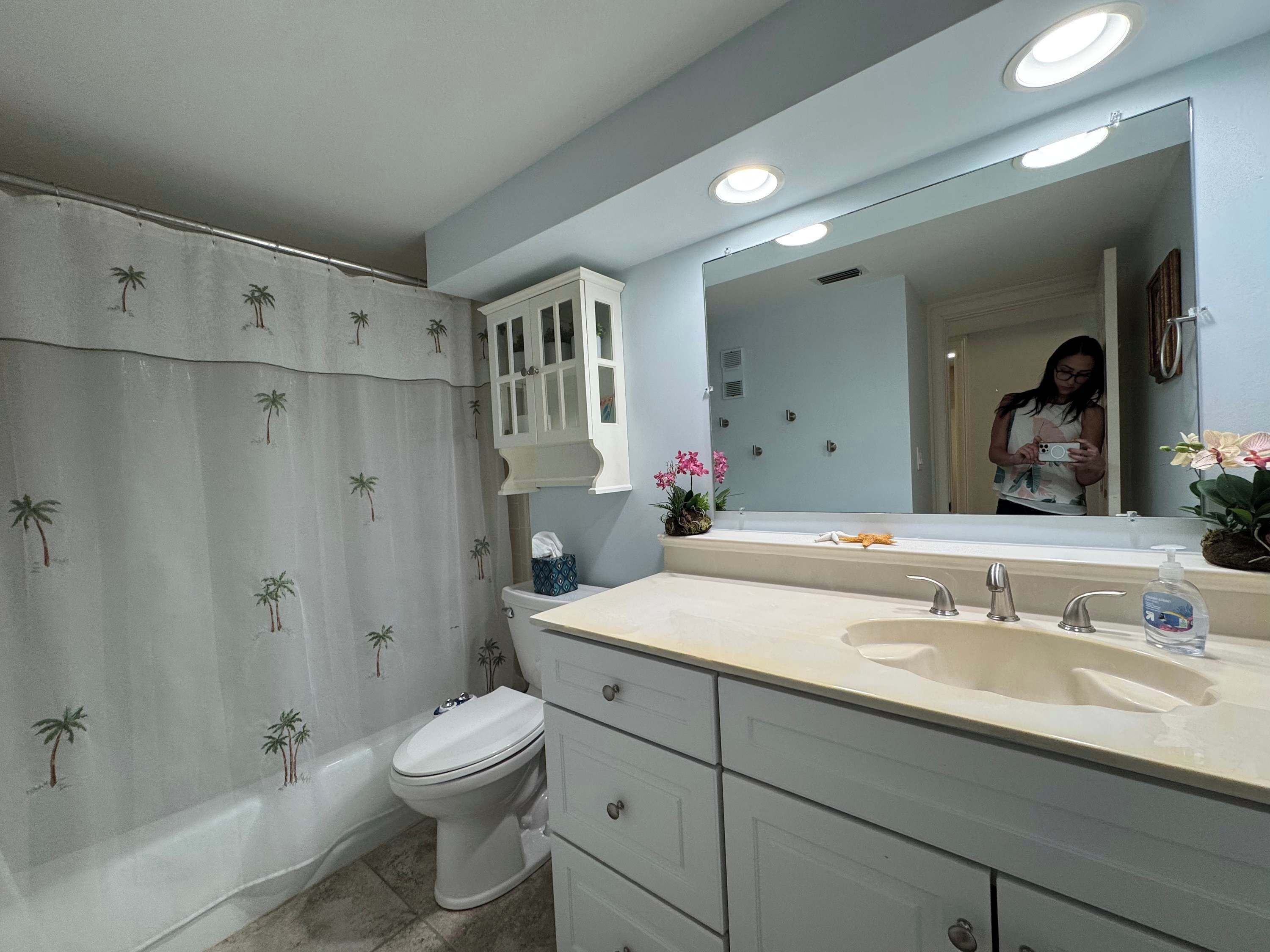 A bathroom with a toilet, a sink with a mirror, and a shower curtain with palm tree patterns.