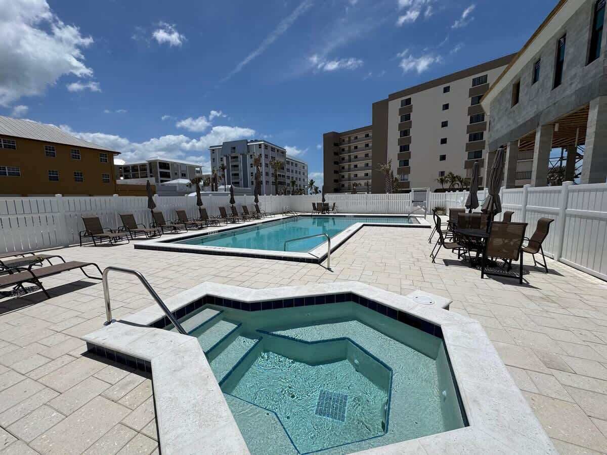 Un espace piscine comprenant un jacuzzi, des chaises longues et une clôture blanche.