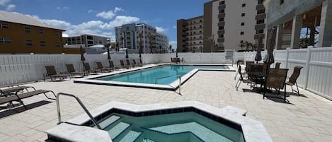 A pool area with a hot tub, lounge chairs, and a white fence.