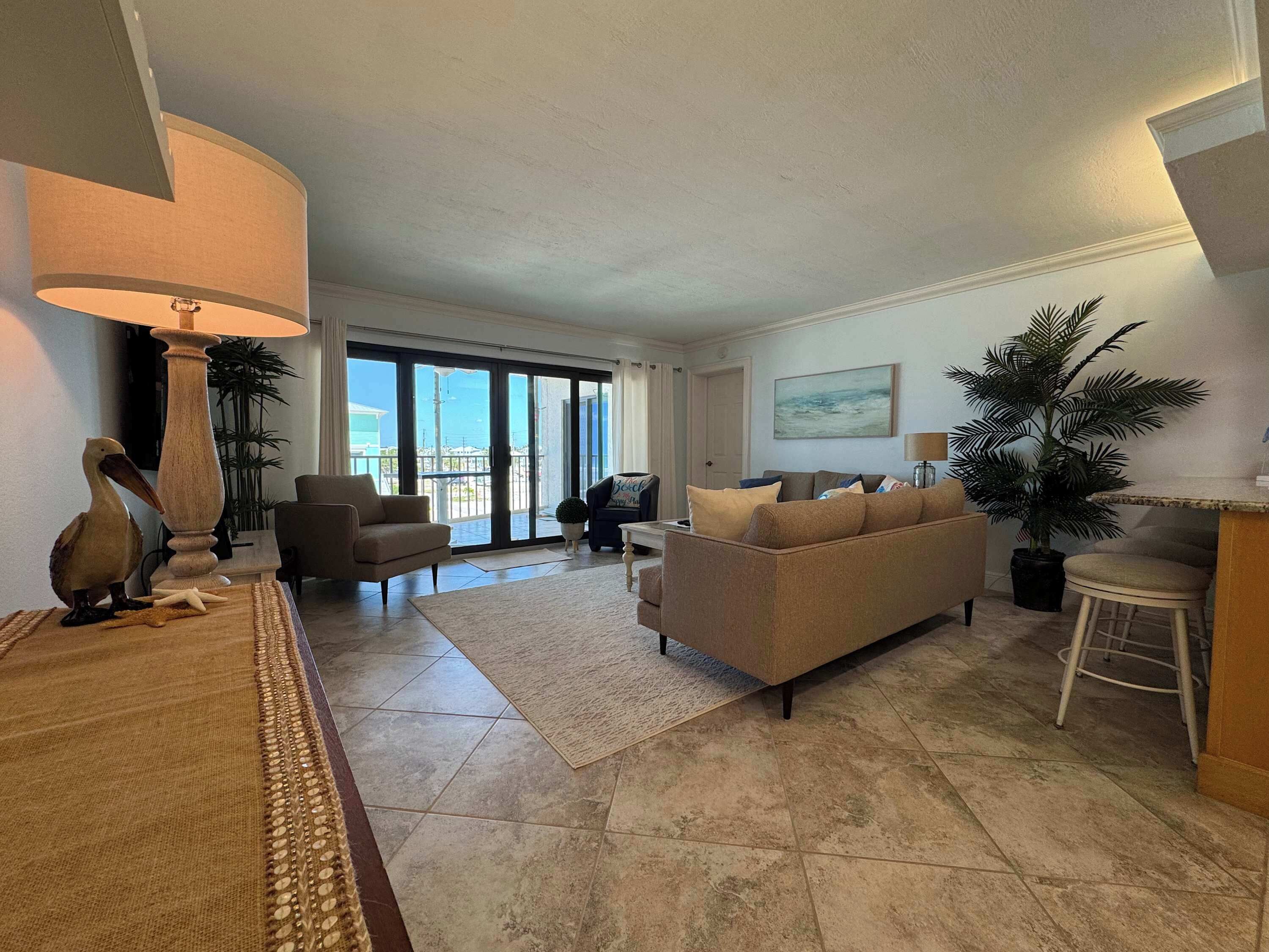A living room with a sofa, armchairs, a lamp, and a view through a glass door.