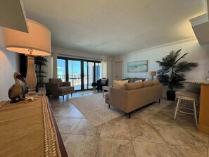 Ein Wohnzimmer mit einer Couch, Sesseln, einer Lampe und Blick durch eine Glastür.