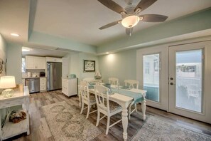 A kitchen with white cabinets, a refrigerator, and a dining area with a table and chairs. - 214 Pearl Main Pet Friendly Cottage near Beach (Fort Myers Beach)