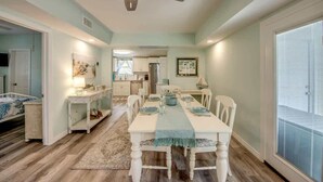 Un comedor con una mesa dispuesta para cuatro personas, un ventilador de techo y vistas a la cocina.