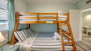Una cama litera con ropa de cama a rayas, una mesita de noche con una lámpara y una ventana con cortinas.