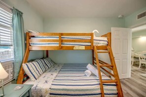 Ein Stockbett mit gestreifter Bettwäsche, ein Nachttisch mit Lampe und ein Fenster mit Vorhängen.