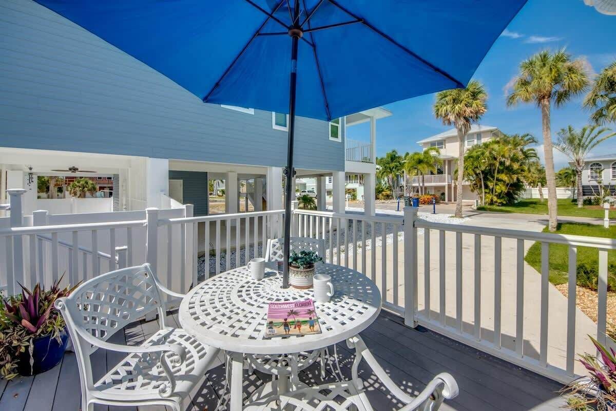A covered outdoor area with a table and chairs, surrounded by white railings and palm trees.