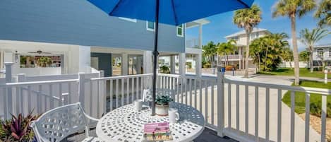A covered outdoor area with a table and chairs, surrounded by white railings and palm trees.