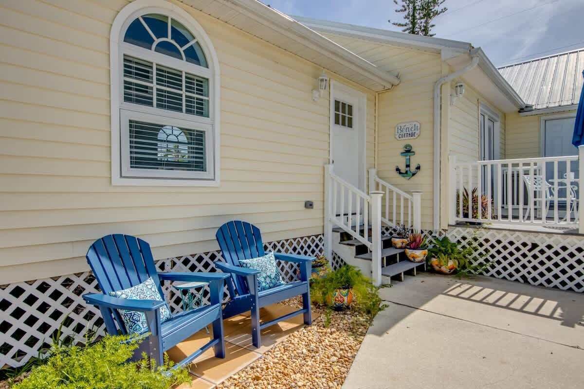 Ein Cottage mit Veranda, zwei Adirondack-Stühlen, einem Schild mit der Aufschrift 'Beach Cottage' und einer kleinen Treppe, die zum Eingang führt.