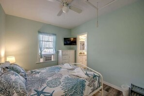 A bedroom with a bed, a ceiling fan, a window with blinds, a television, and a bathroom visible through an open door. - 214 Pearl Main Pet Friendly Cottage near Beach (Fort Myers Beach)