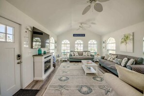 A spacious living room with a large window, a ceiling fan, and a sign reading 'BEACH HOUSE'. - 214 Pearl Main Pet Friendly Cottage near Beach (Fort Myers Beach)