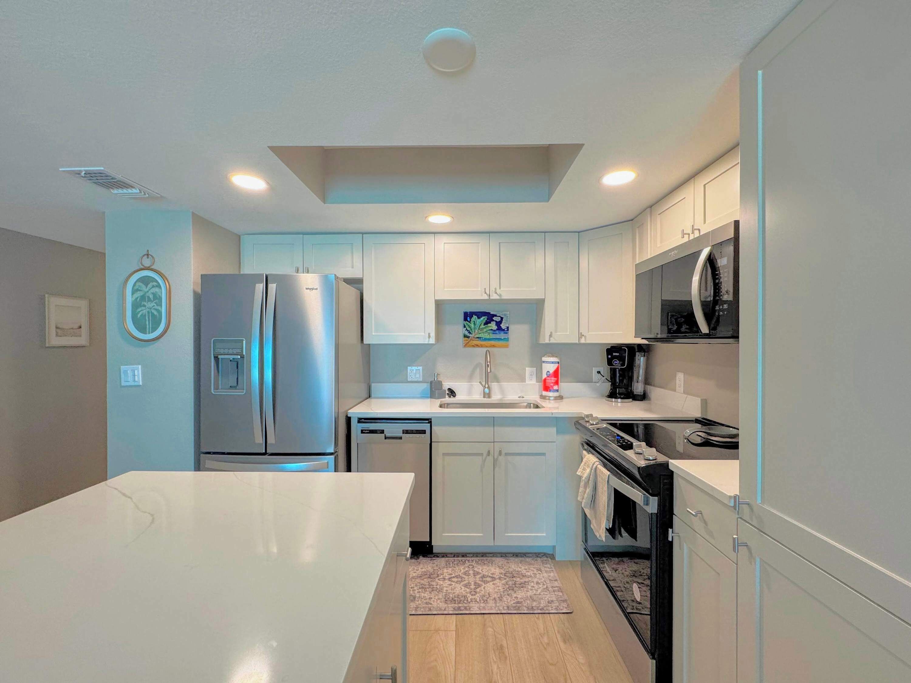 A modern kitchen with white cabinetry, a stainless steel refrigerator, a microwave, and a dishwasher.